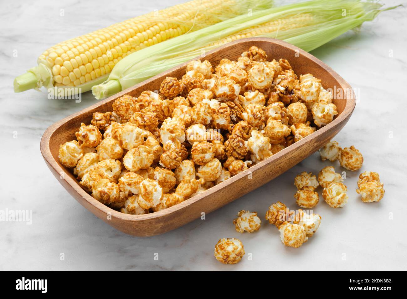 Holzschüssel mit Karamell-Popcorn, frische Maiskolben auf dem Hintergrund. Stockfoto