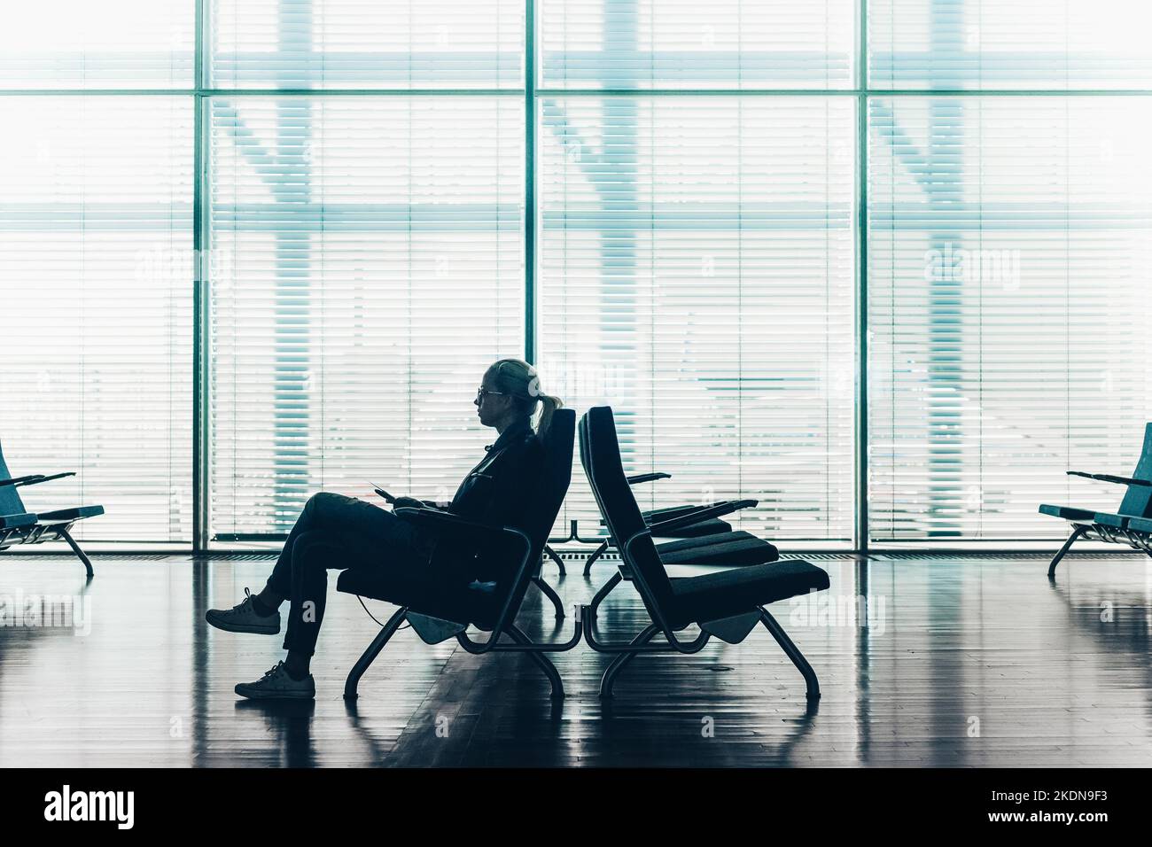 Silhouette einer Frau auf der Durchreise mit dem Smartphone, die am Flughafeneingang wartet. Horisontale Zusammensetzung. Konzentrieren Sie sich auf den Passanten. Stockfoto