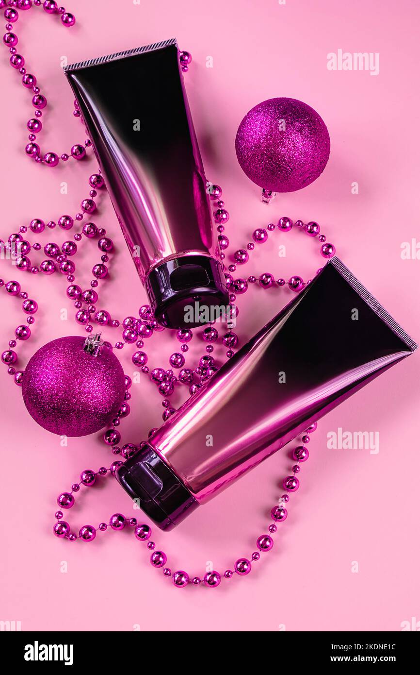 Set aus schwarzen und rosa Squeeze Kosmetikflaschen und Weihnachtsdekorationen auf pastellfarbenem Hintergrund. Lotion oder Creme in Luxus-Kosmetikschlauch. Nicht gebrandete Produkte Stockfoto