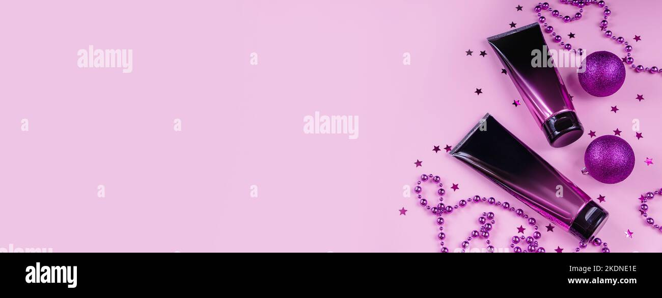 Set aus schwarzen und rosa Squeeze Kosmetikflaschen und Weihnachtsdekoration auf pastellfarbenem Hintergrund. Hautpflegecreme in luxuriöser Kosmetikröhre. Nicht markengebrandeter Adver Stockfoto