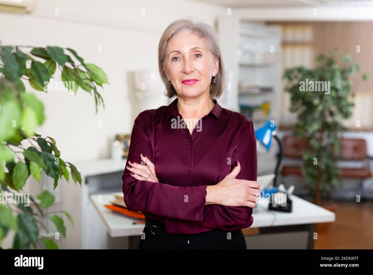 Erfolgreiche, selbstbewusste ältere Geschäftsfrau mit gekreuzten Armen im Amt Stockfoto