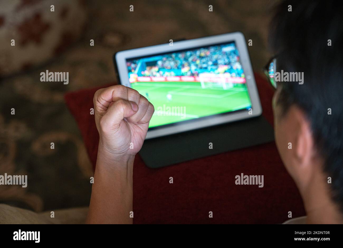 Mann mit der Faust nach oben, während er Fußballspiele auf dem digitalen Tablet auf der Couch ansieht. Stockfoto