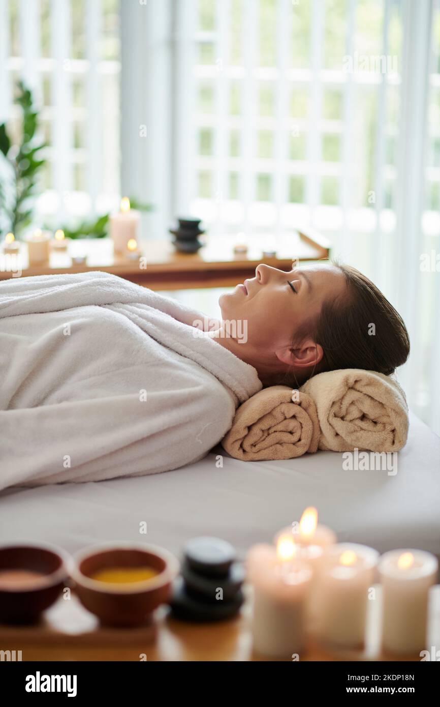 Frau im Bademantel, die sich im Schönheitssalon auf dem Bett ausruhte, nachdem sie einen entspannenden Spa-Eingriff gemacht hatte Stockfoto