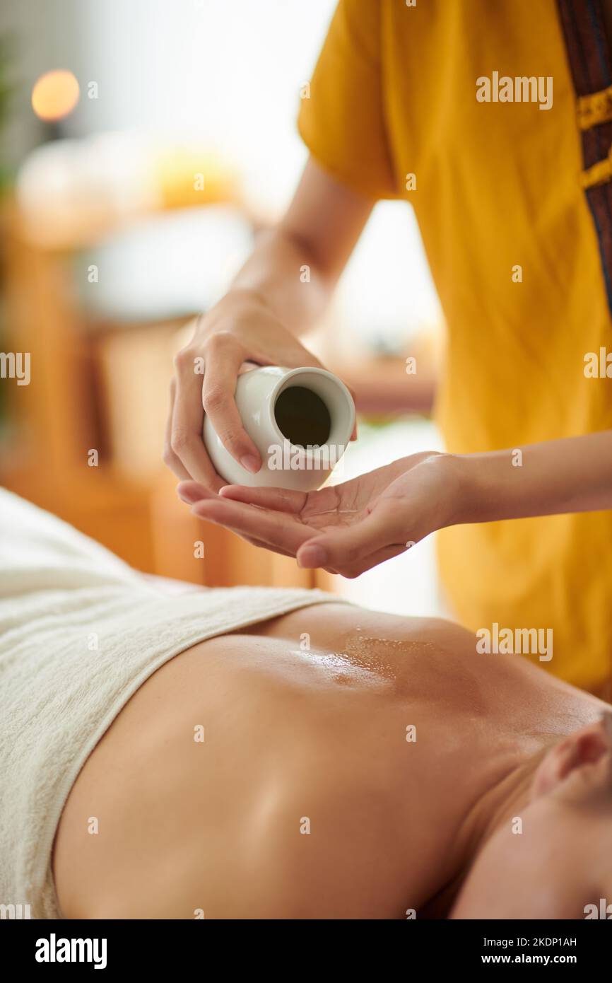 Hände der Masseurin, die Massageöl auf den Rücken der Frau auftragen Stockfoto