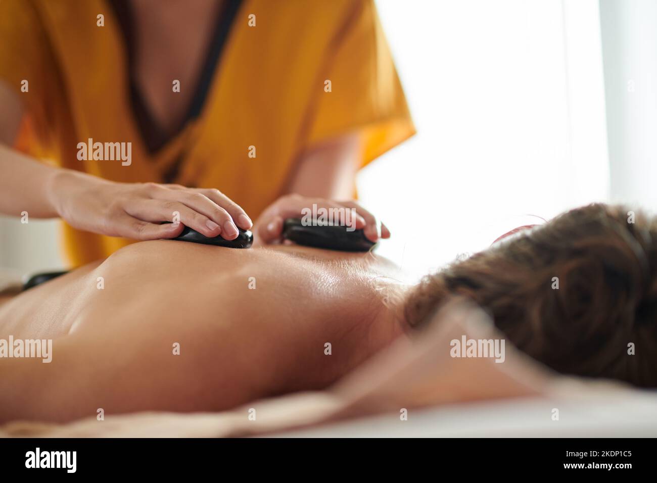 Nahaufnahme einer Frau, die den Klienten mit heißen Basaltsteinen massiert Stockfoto