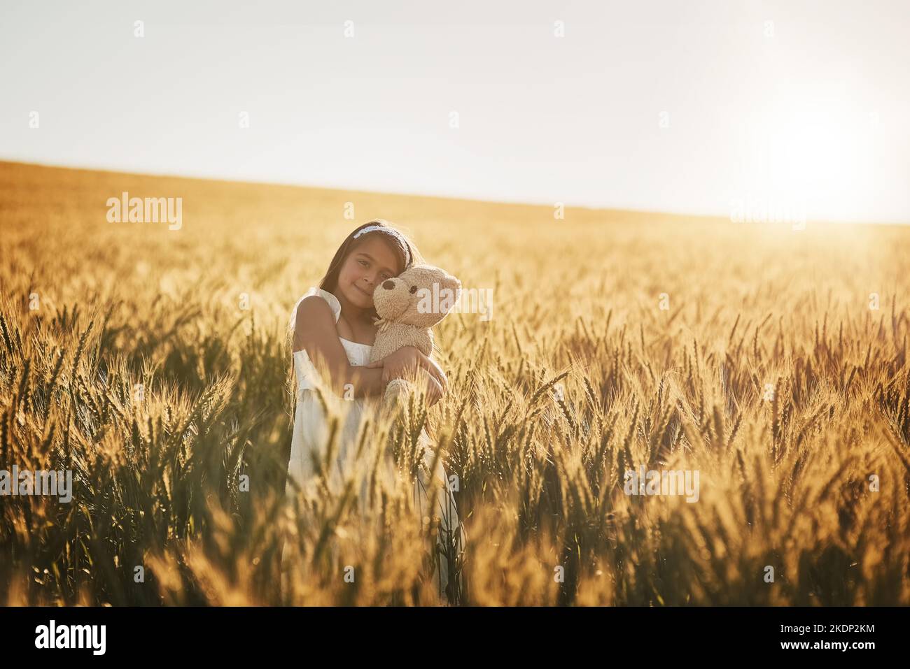 Die wahre Liebe ihrer Kindheit. Ein süßes kleines Mädchen, das mit ihrem Teddybär auf einem Kornfeld spielt. Stockfoto