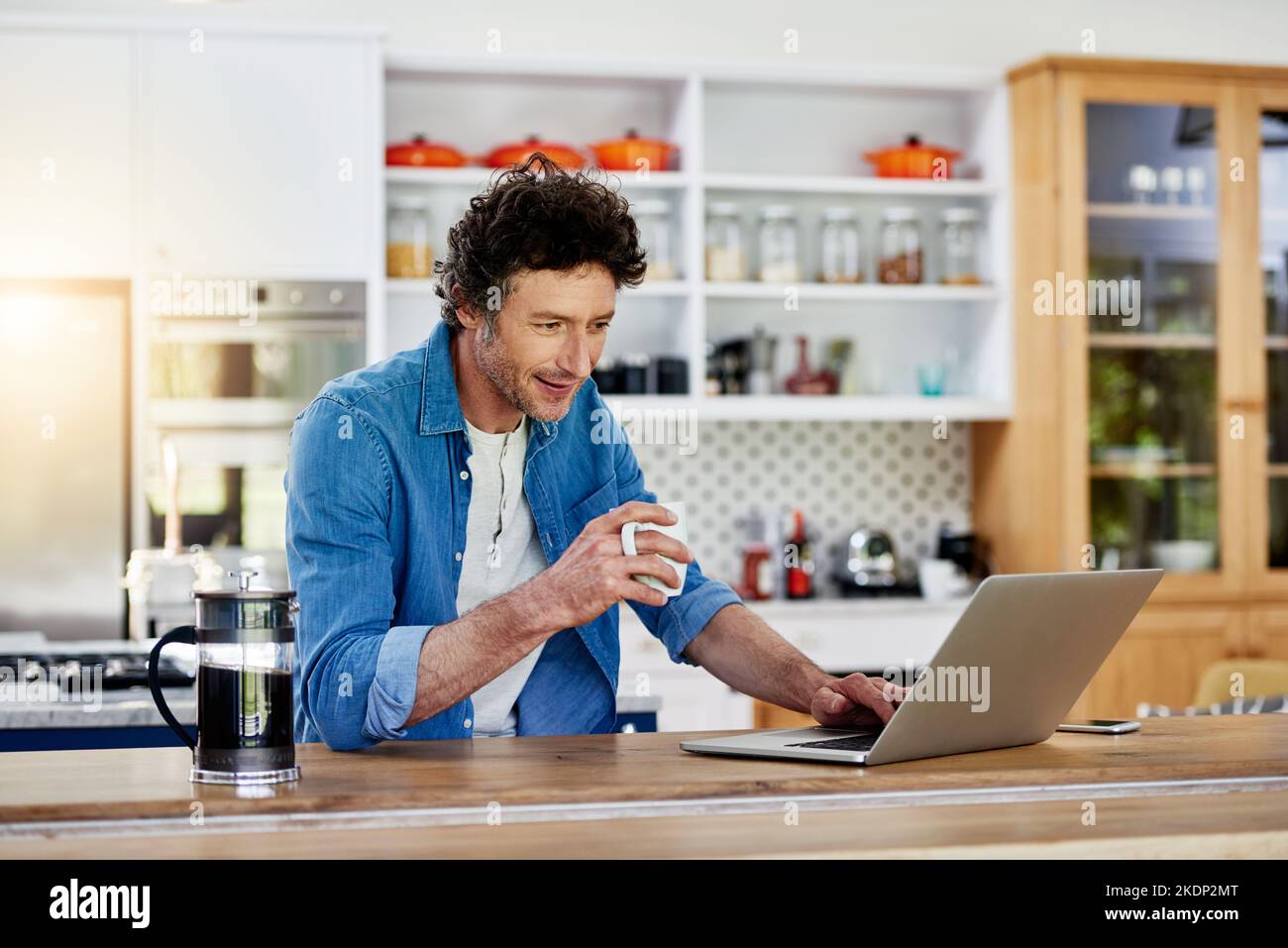Kaffee und WLAN sind eine tolle Kombination. Ein Junggesellen mit seinem Laptop, während er eine Tasse Kaffee in der Küche genießt. Stockfoto