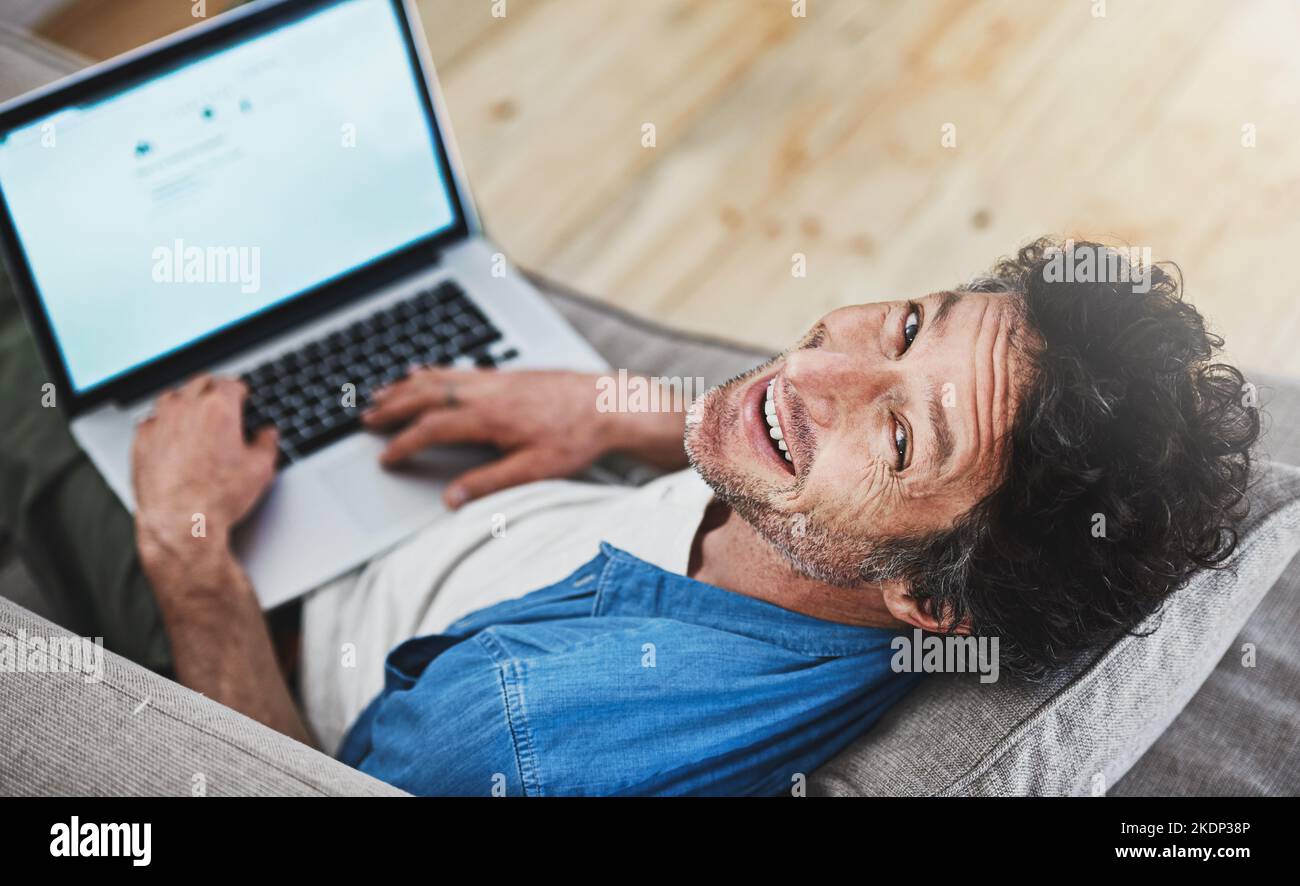 Wer braucht ein Wifey, wenn man WiFi hat. Hochwinkelporträt eines glücklichen Junggesellen, der sich mit seinem Laptop auf dem Sofa entspannt. Stockfoto