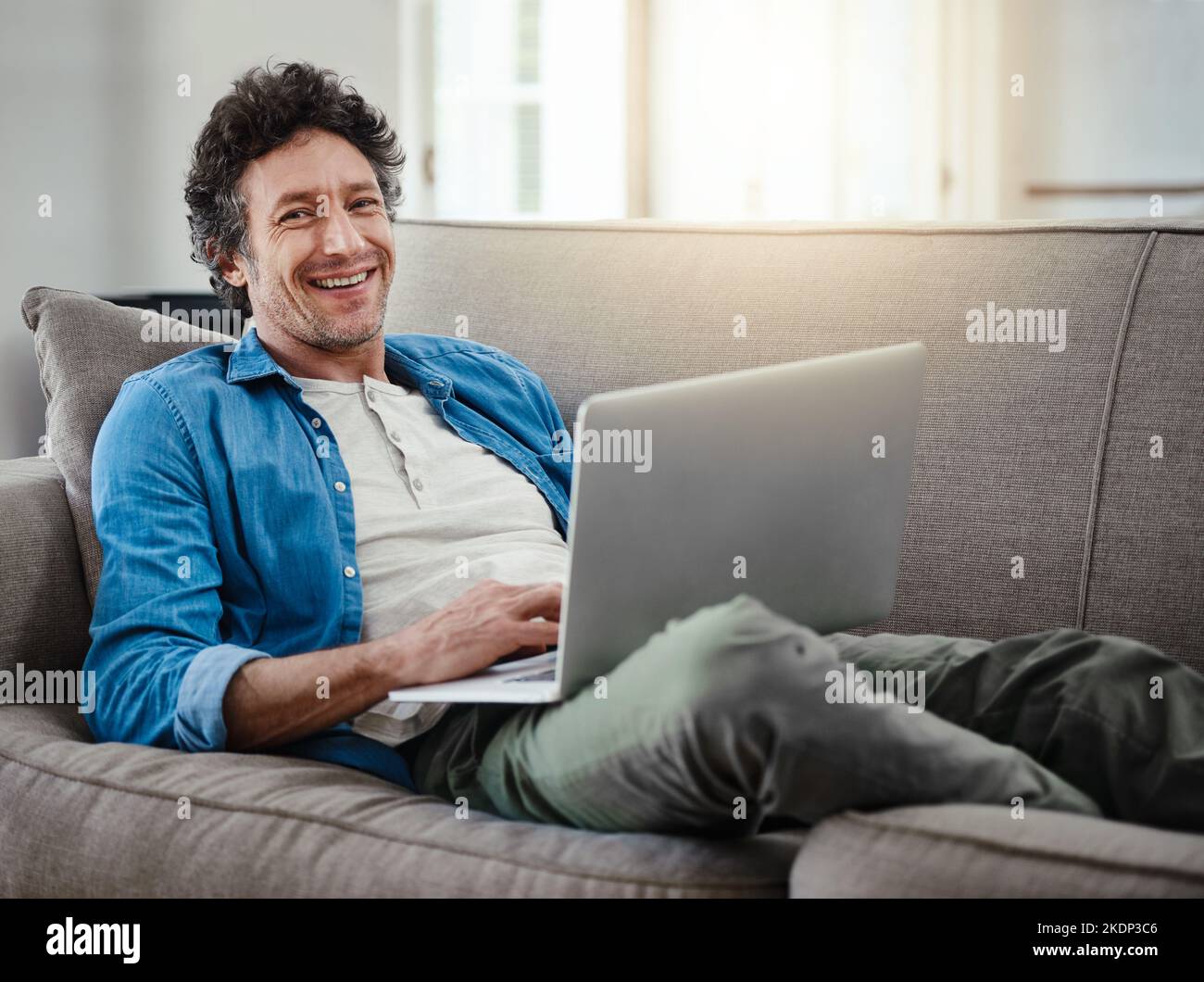 Zeit, die Sie gerne verschwenden, wird nie wirklich verschwendet. Porträt eines glücklichen Junggesellen, der sich mit seinem Laptop auf dem Sofa entspannt. Stockfoto