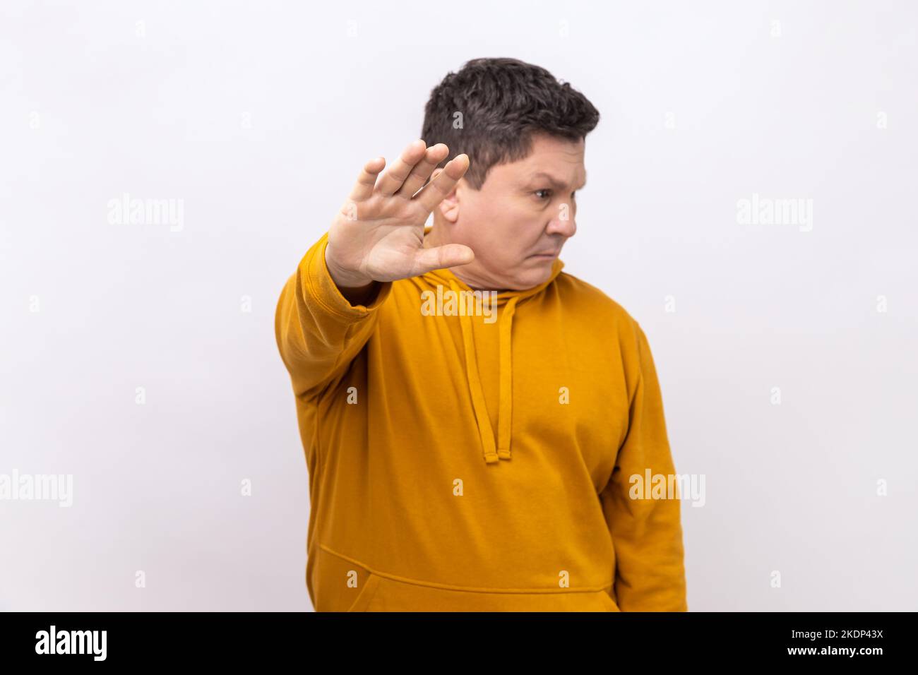Porträt eines Mannes mittleren Alters mit Stoppschild, mit drehendem Gesicht stehend, was Vorsicht bedeutet, um Gefahren oder Fehler zu vermeiden, mit einem Hoodie im urbanen Stil. Innenaufnahme des Studios isoliert auf weißem Hintergrund. Stockfoto