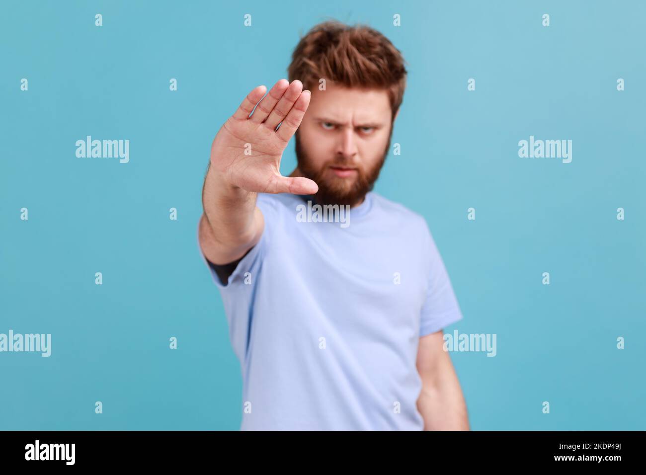 Porträt eines strengen bärtigen Mannes, der ein Stoppschild an der Kamera zeigt, mit runzelndem Gesicht und herrlicher Ausdruckskraft steht, was Vorsicht bedeutet, um Gefahren oder Fehler zu vermeiden. Innenaufnahme des Studios isoliert auf blauem Hintergrund Stockfoto