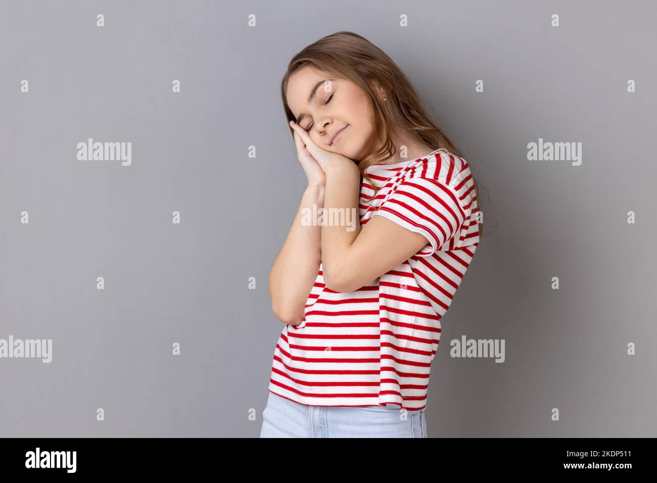 Ich brauche Ruhe. Porträt eines kleinen Mädchens in gestreiftem T-Shirt, das gähnend und den Mund mit der Hand bedeckt, sich erschöpft fühlt, Schlafmangel. Innenaufnahme des Studios isoliert auf grauem Hintergrund. Stockfoto