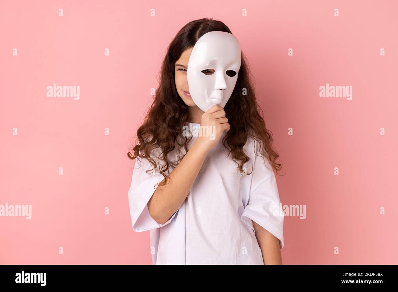 Porträt eines dunkelhaarigen kleinen Mädchens mit weißem T-Shirt im Gesicht, mit runzelndem Gesicht, multipler Persönlichkeitsstörung. Innenaufnahme des Studios isoliert auf rosa Hintergrund. Stockfoto