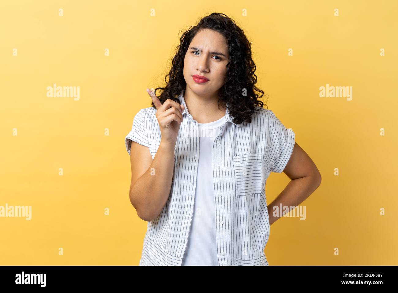 Porträt einer ernsthaften strengen Frau mit dunklen welligen Haaren, die mit dem Finger auf die Kamera zeigt und mit unzufriedenem, verdächtigem Ausdruck aussieht. Innenaufnahme des Studios isoliert auf gelbem Hintergrund. Stockfoto