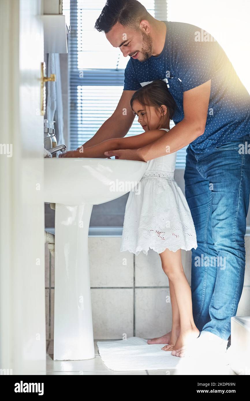 Ein Vater hilft seiner kleinen Tochter, sich die Hände am Waschbecken im Badezimmer zu waschen. Stockfoto