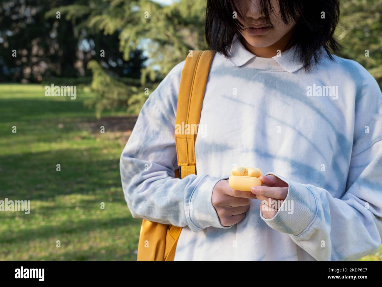 Unbekanntes Mädchen mit gelbem Rucksack und Ohrhörern an den Händen im Park. Stockfoto