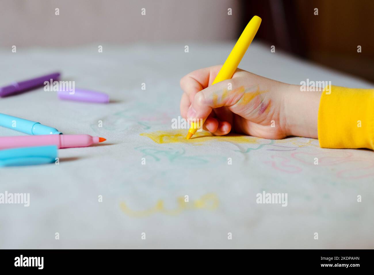 Die Kinderhandzeichnung mit gelbem Filzstift auf der grauen Polsterung der Couch. Tägliches Leben schmutziger Fleck für Wasch- und Sauberkonzept Stockfoto