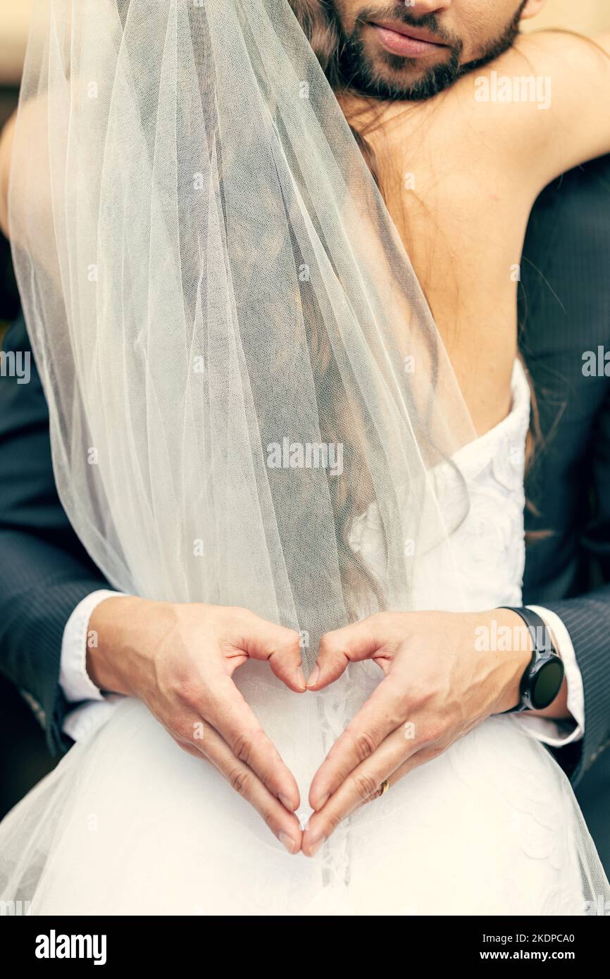 Hand, Herz und Braut und Bräutigam umarmen sich bei ihrer Hochzeit, freuen sich und entspannen sich, während sie einen intimen Moment teilen. Hände, Liebe und Paar feiern ihre Stockfoto