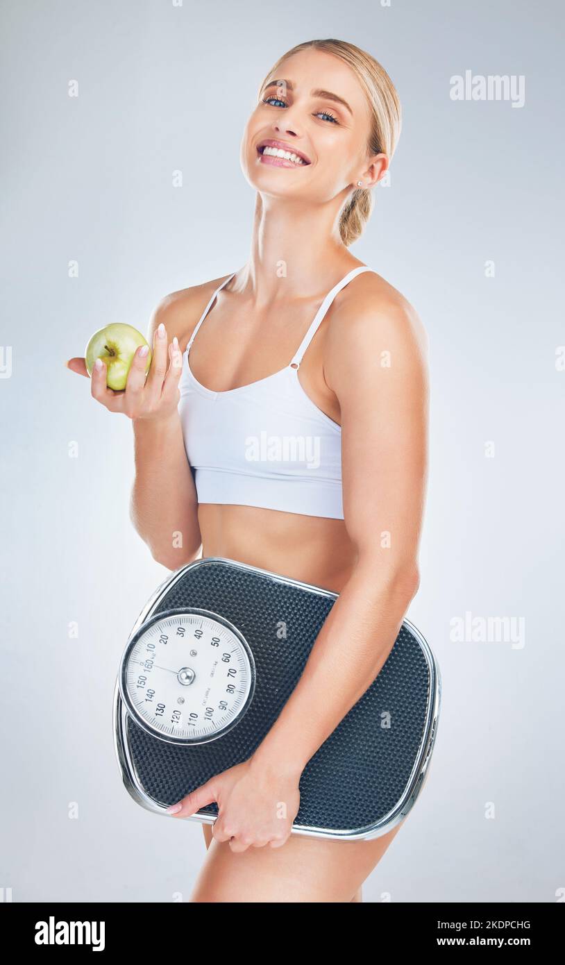 Gesundheit, Gewicht verlieren und Frau mit Apfel und Waage für Körperziel, Motivation und Ernährung vor grauem Studiohintergrund. Essen, glücklich und Stockfoto