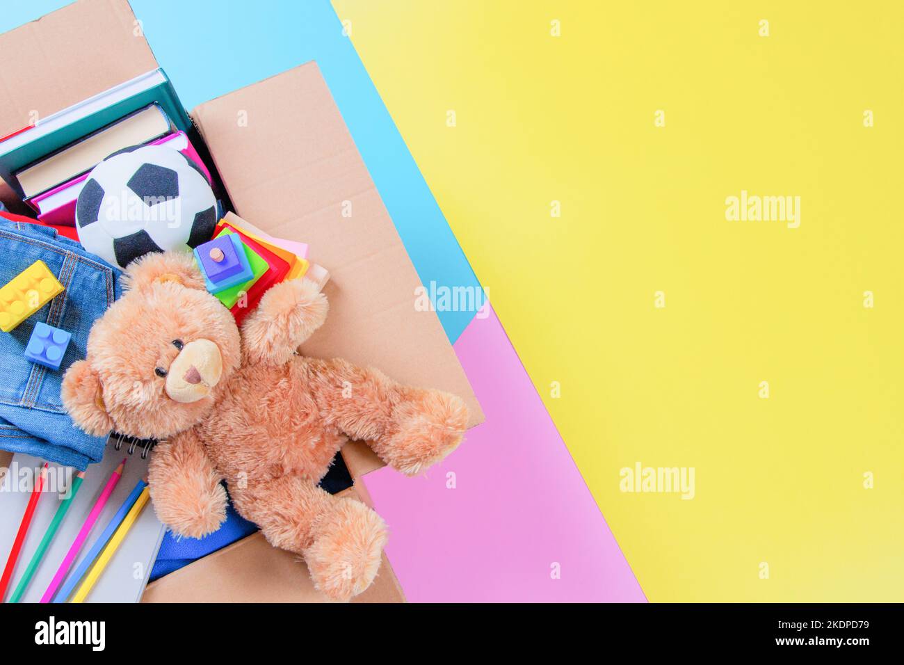 Spendenbox mit Kinderspielzeug, Büchern, Kleidung für wohltätige Zwecke auf buntem Gelb, Rosa, hellblauem Hintergrund. Draufsicht Stockfoto