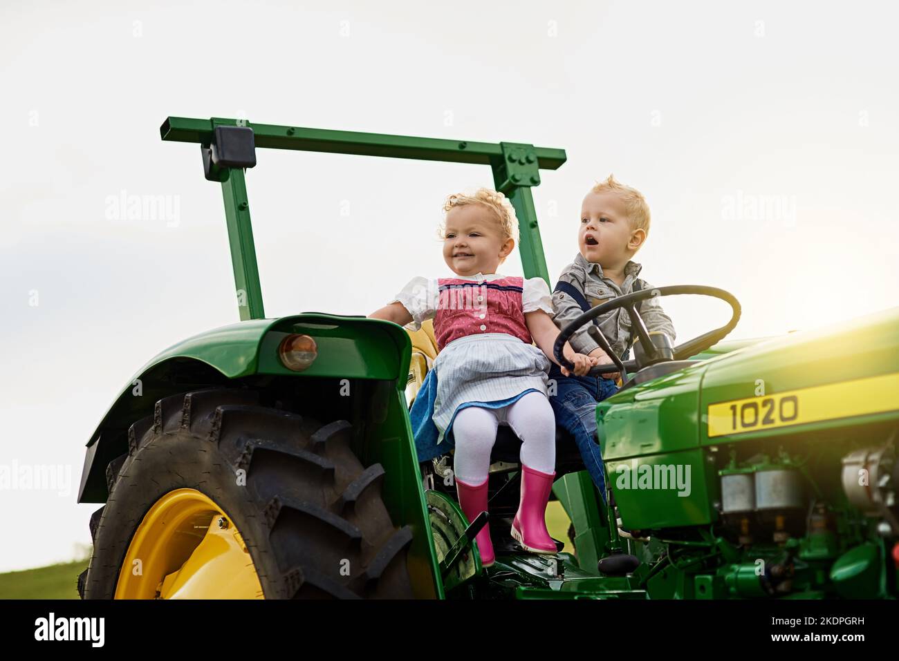 Die nächste Generation von Bauern. Zwei entzückende Kinder, die auf einem Traktor zusammen auf einem Bauernhof reiten. Stockfoto