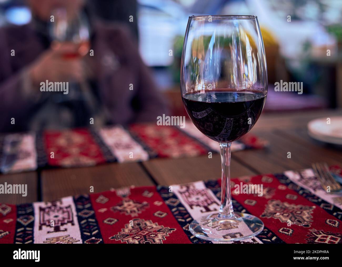 Ein Glas Rotwein auf einem Restauranttisch mit Serviettenreflexen im Glas. Tischunterlage in einem Restaurant mit krimtatarischer Küche Stockfoto