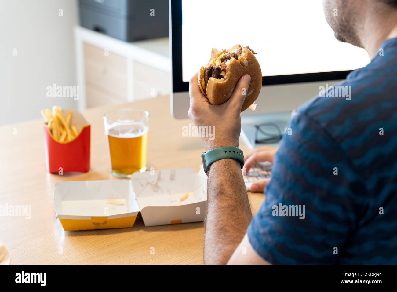 Mann, der vor dem Computer in seinem Büro Fastfood isst Stockfoto