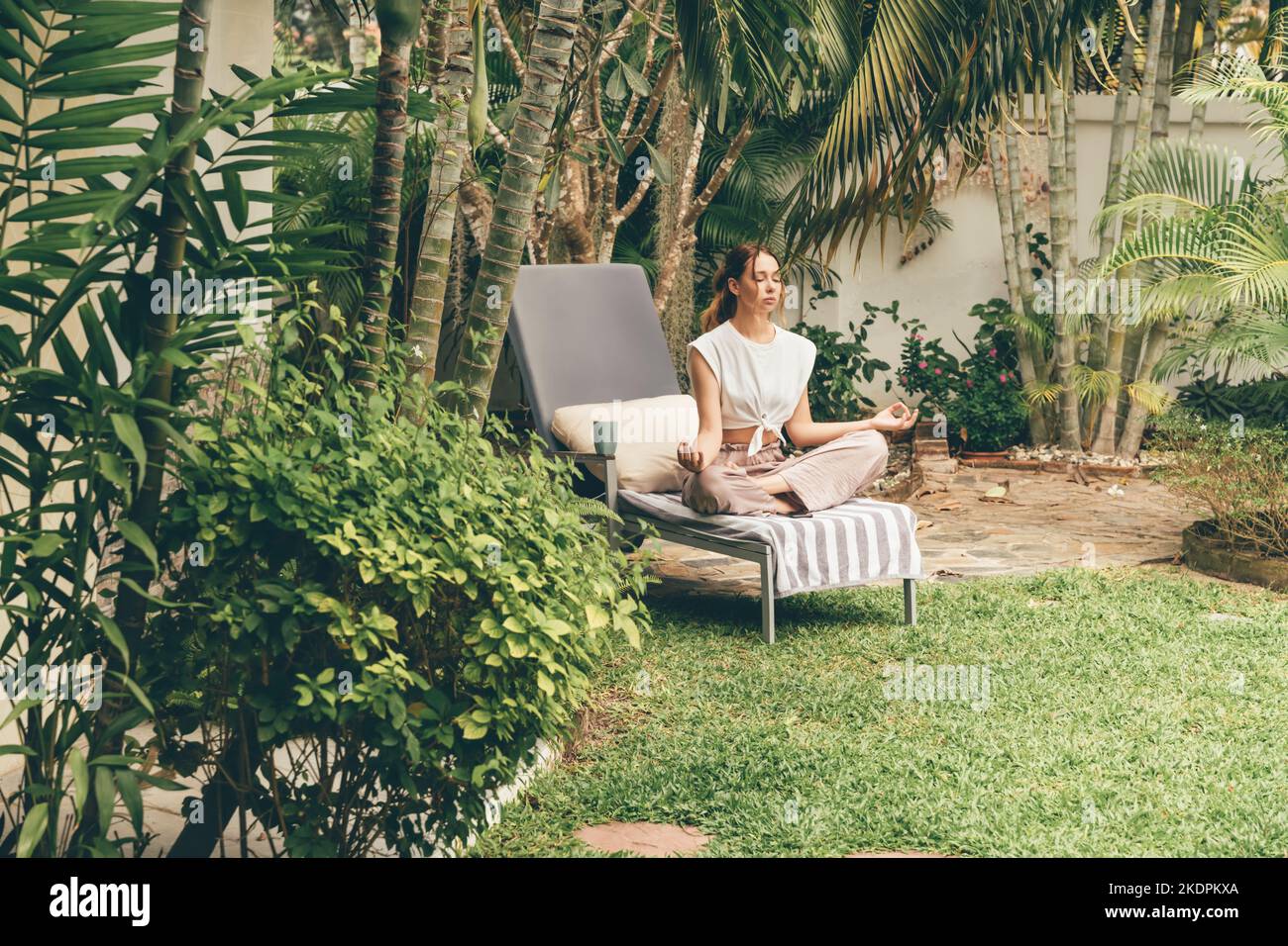 Junge Frau entspannt sich auf einer Sonnenliege im Garten. Meditation im Garten. Stockfoto
