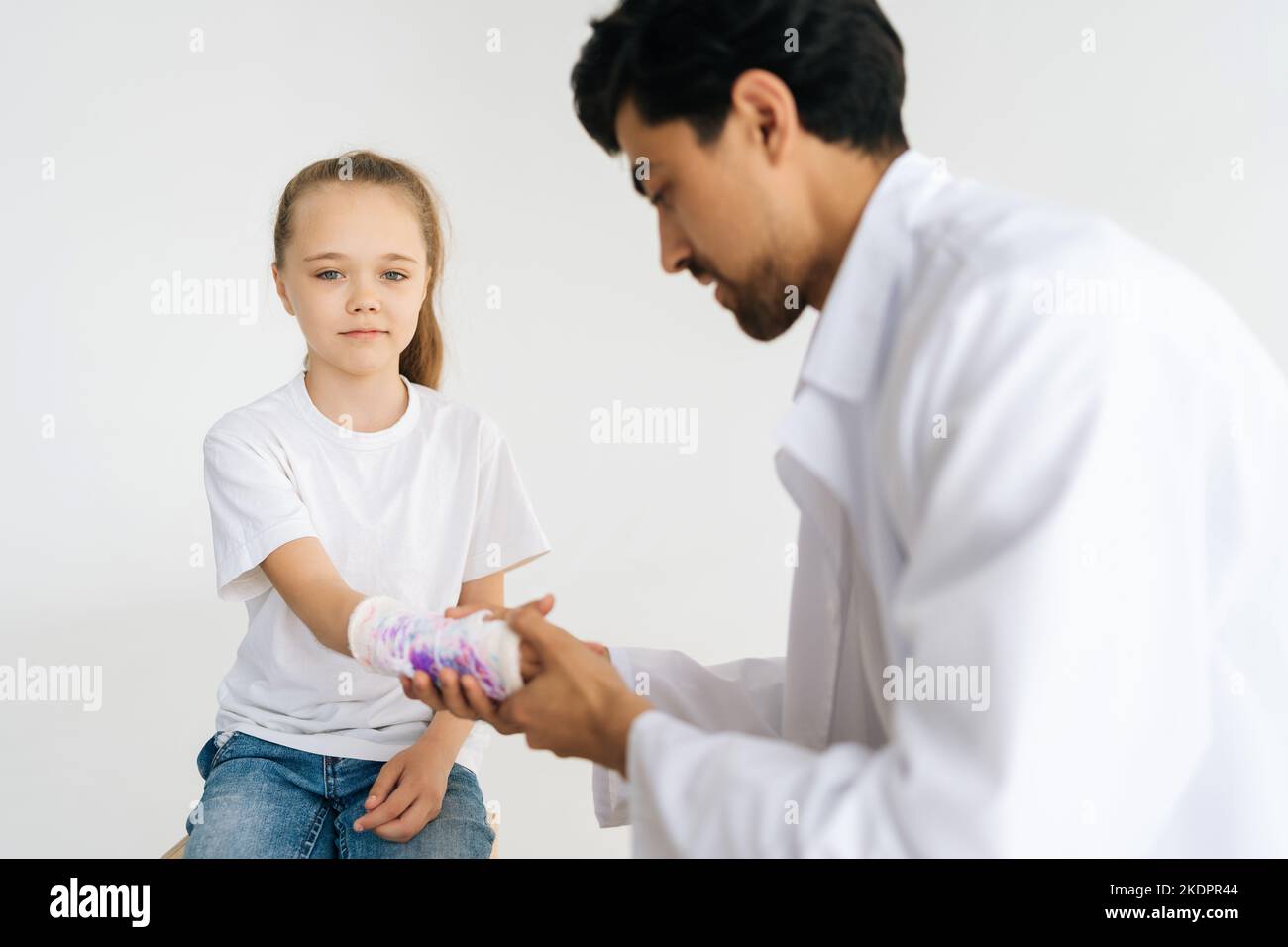 Studio Portrait von niedlichen blonden kleinen Mädchen mit gebrochener Hand in weißen Gips Verband gewickelt immer medizinische Versorgung des Kinderarztes männlichen Arzt. Stockfoto