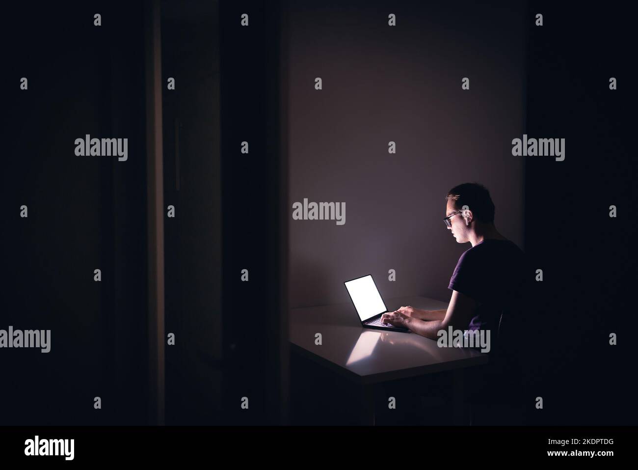 Nachtarbeit mit Laptop in dunklem Home Office-Zimmer. Junger Mann mit Notebook-Computer. Coder, Programmierer, Hacker, freiberuflicher digitaler Redakteur oder Student. Stockfoto