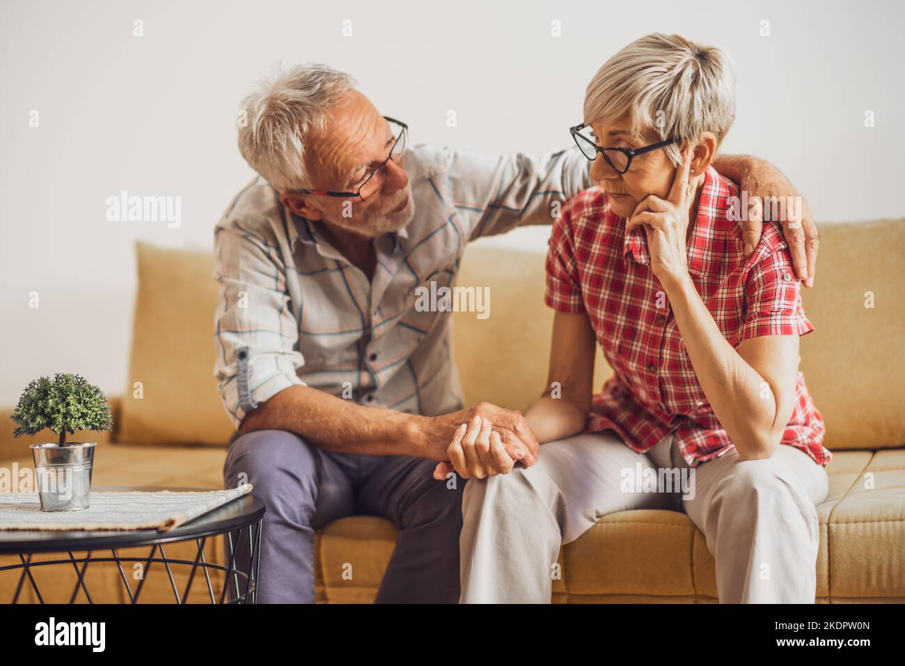 Seniorenpaar sitzt im Wohnzimmer. Die Frau ist traurig und besorgt und der Mann tröstet sie. Stockfoto