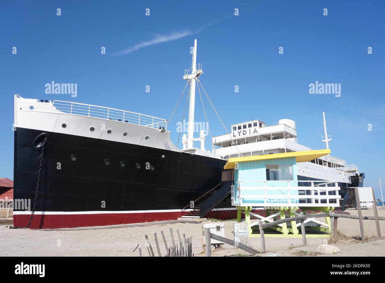 Port-Barcarès, Frankreich - 2022. Oktober; ehemaliges Kreuzschiff Le Lydia am Strand neben dem farbenfrohen Rettungsschwimmerturm vor dem Hintergrund des blauen Himmels Stockfoto