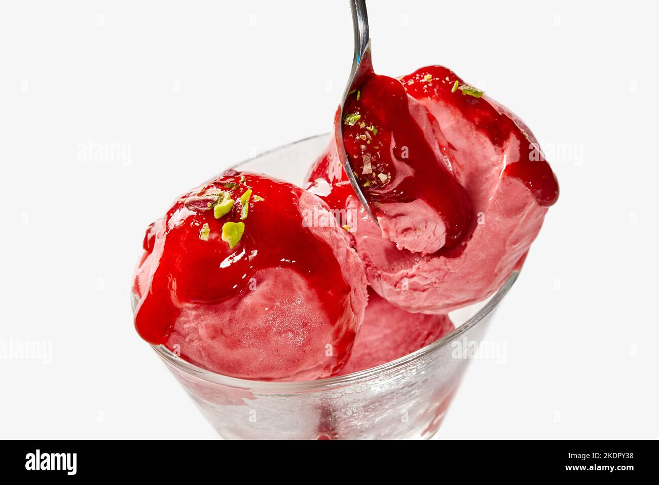 Kugeln Fruchteis mit Beerenmarmelade und Pistazien in Glasschüssel mit Löffel gekrönt Stockfoto
