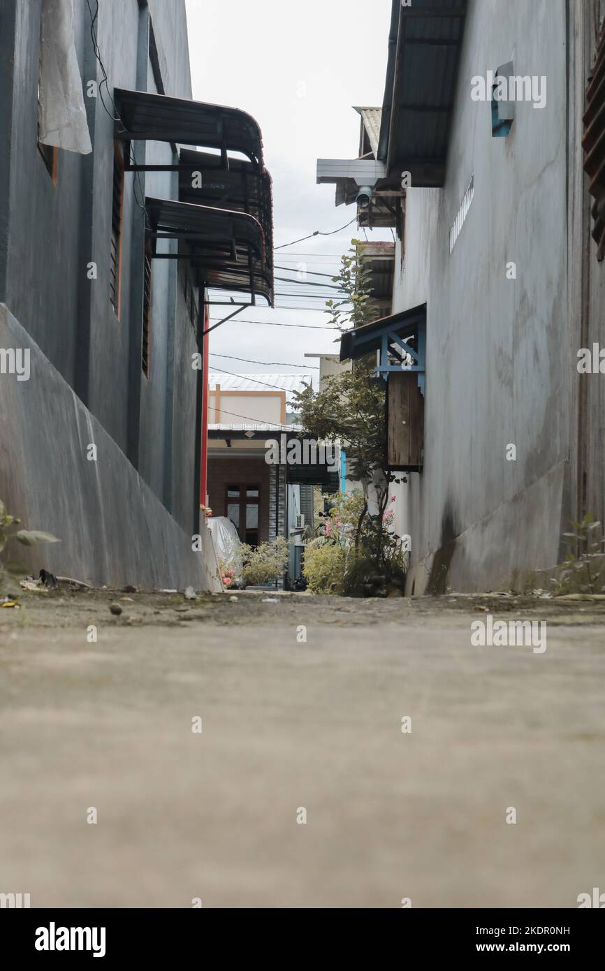 Eine schmale Gasse zwischen 2 Häusern mit Zementwänden im Stil eines Froschaugen-Fotos und davor befindet sich ein Haus Stockfoto