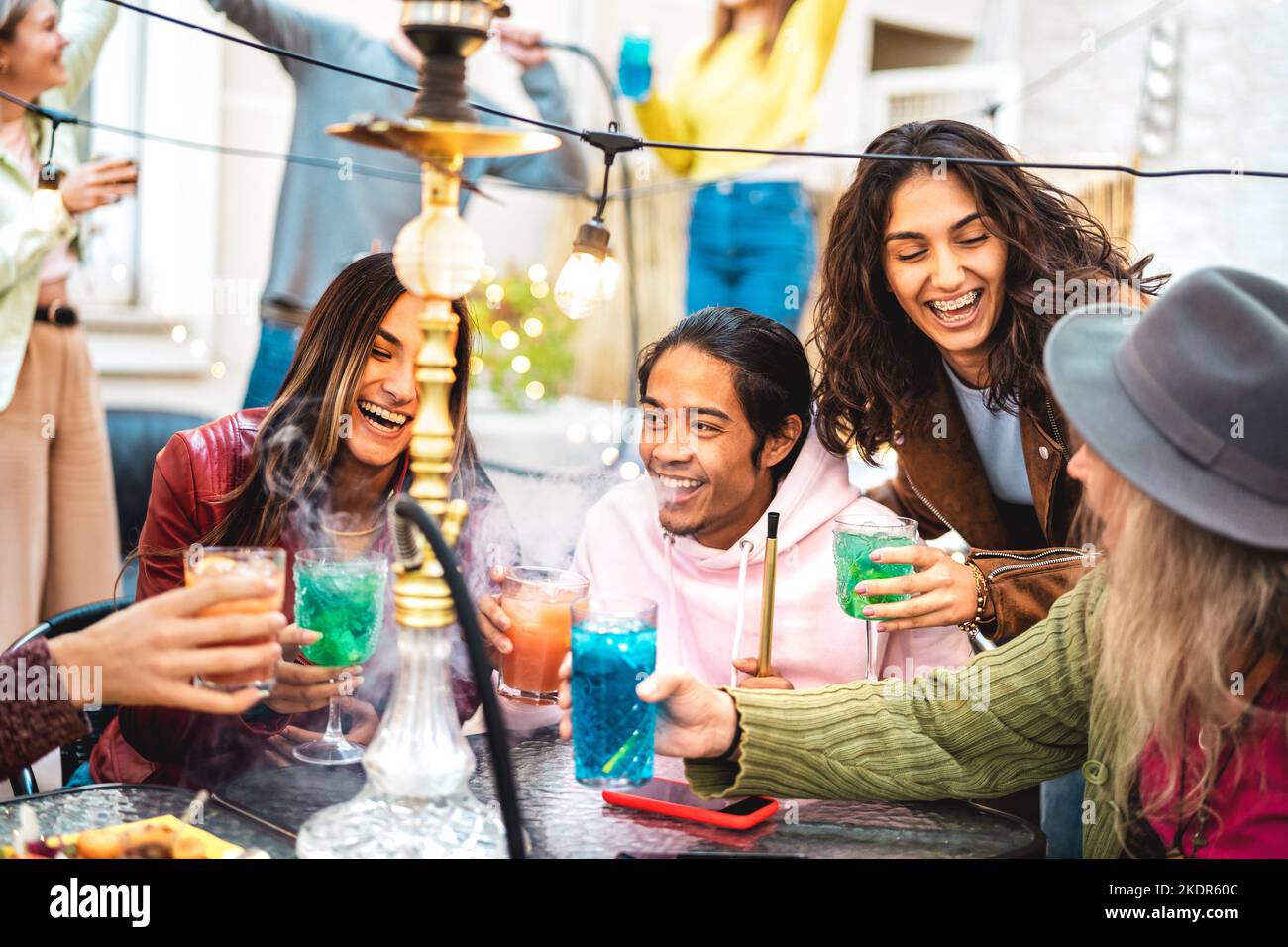 Fröhliche trendige Freunde, die Spaß beim Cocktailtrinken in der Shisha Bar haben - echte Millennials, die zusammen Getränke im schicken Restaurantgarten toasten - Essen Stockfoto