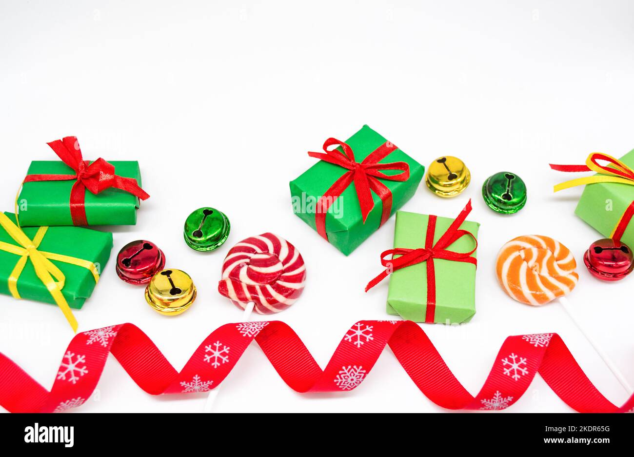 Frohe Festtage: Geschenke mit Lutschern und roten, grünen, goldenen Glocken. Rotes Band auf weißem Hintergrund, Platz zum Kopieren. Das Konzept von Weihnachten, Verkauf. Stockfoto