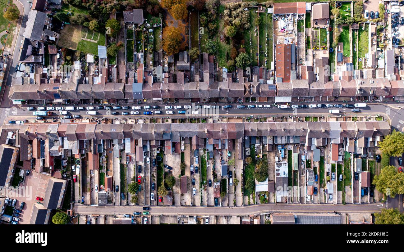 Luftaufnahme direkt über einer langen Stadtstraße, gesäumt von heruntergekommenen Reihenhäusern und Gärten mit anschaufendem Verkehr im Norden Englands Stockfoto