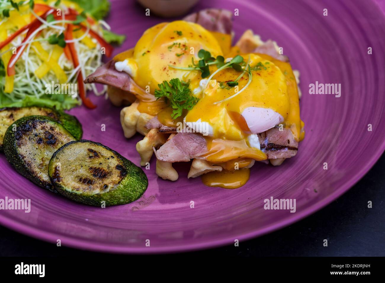 Eier Benedikt (pochierte Eier) auf gegrilltem Schinken mit holland-Sauce auf belgischen Waffeln mit gegrillten Zucchini mit Bananenplatte und einer Tasse Passionssaft Stockfoto