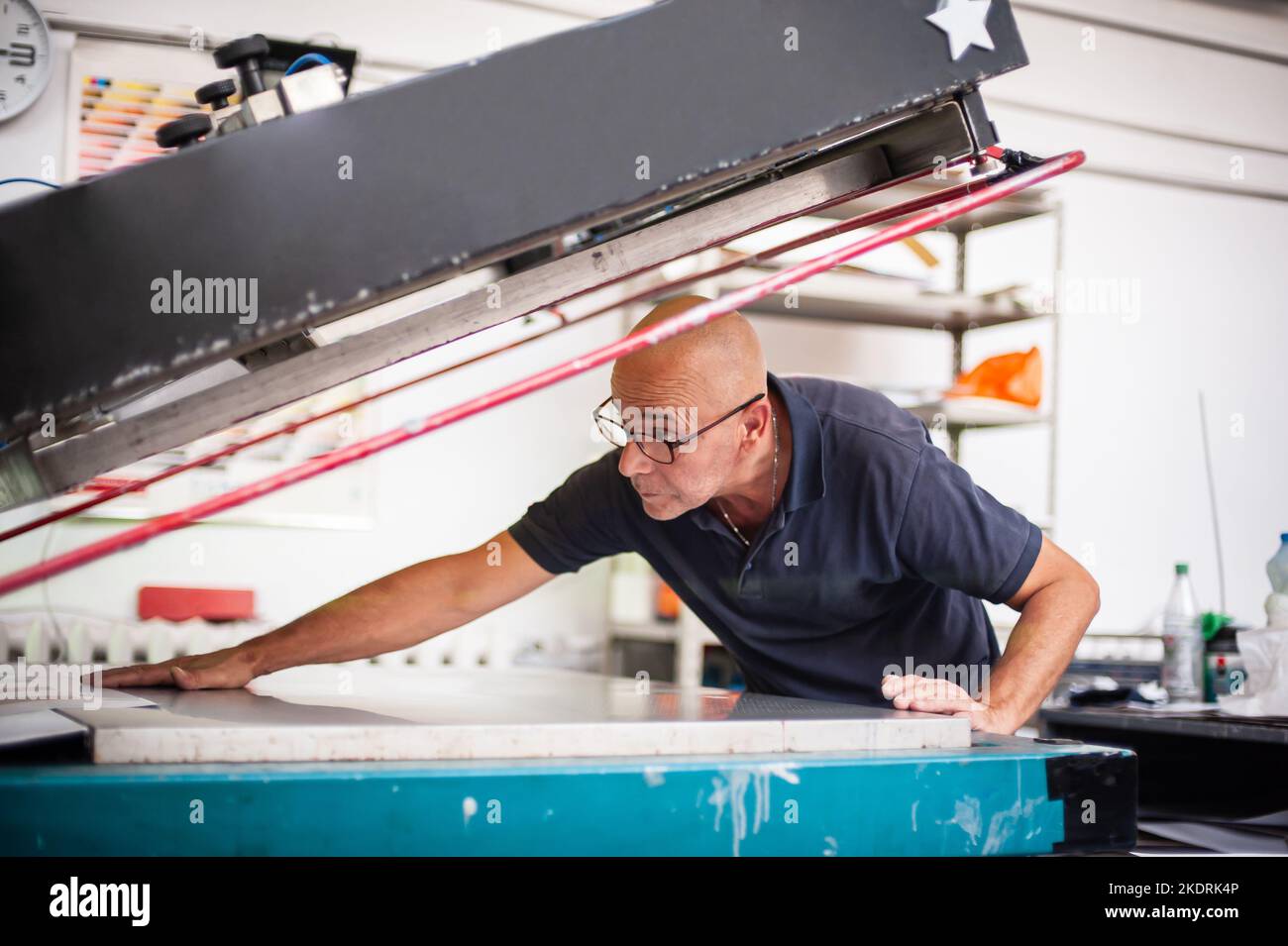 In der Druckerei arbeitet ein erfahrener Techniker an einer Siebdruckmaschine. Produktionsarbeit. Überprüfen Sie die Druckqualität. Stockfoto