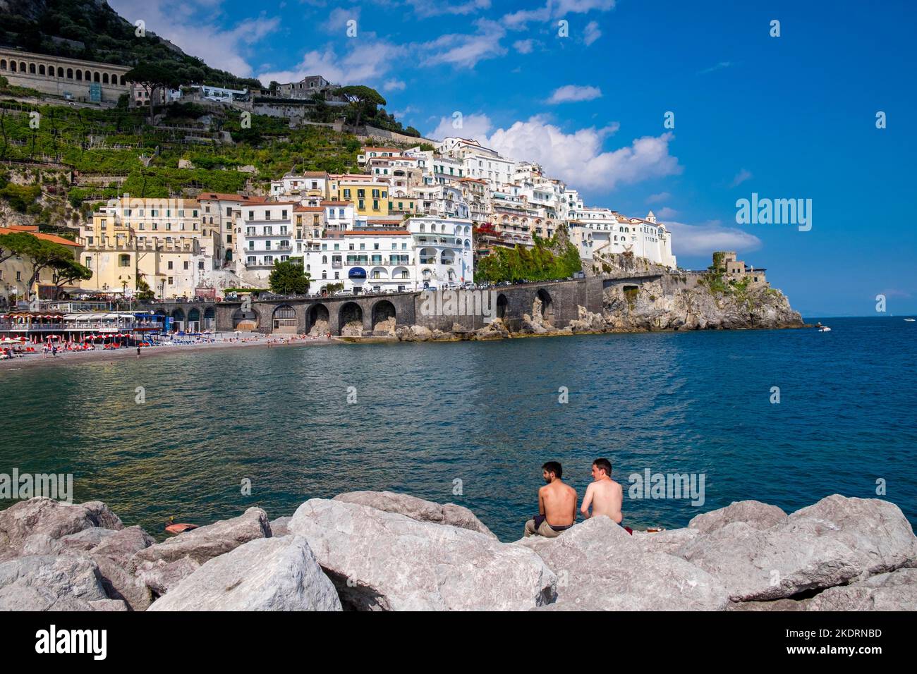 Die Stadt Amalfi an der italienischen Amalfiküste, von der Steinkofel aus gesehen, die den Hafen schützt, mit 2 Schwimmern, die zusehen. Stockfoto