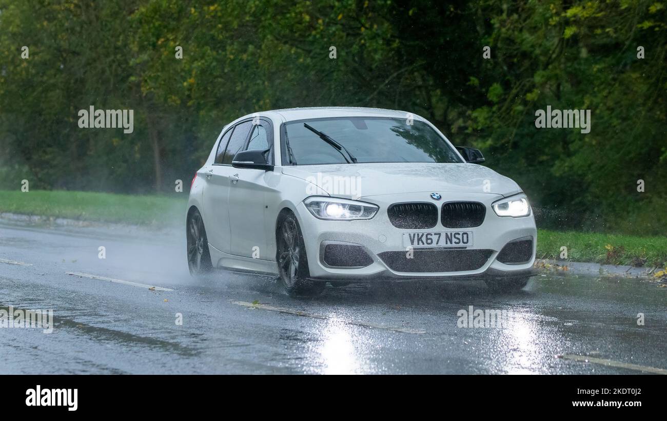 Weißes Fahrzeug der BMW 1 Serie 2017, das im Regen auf nasser Straße fährt Stockfoto