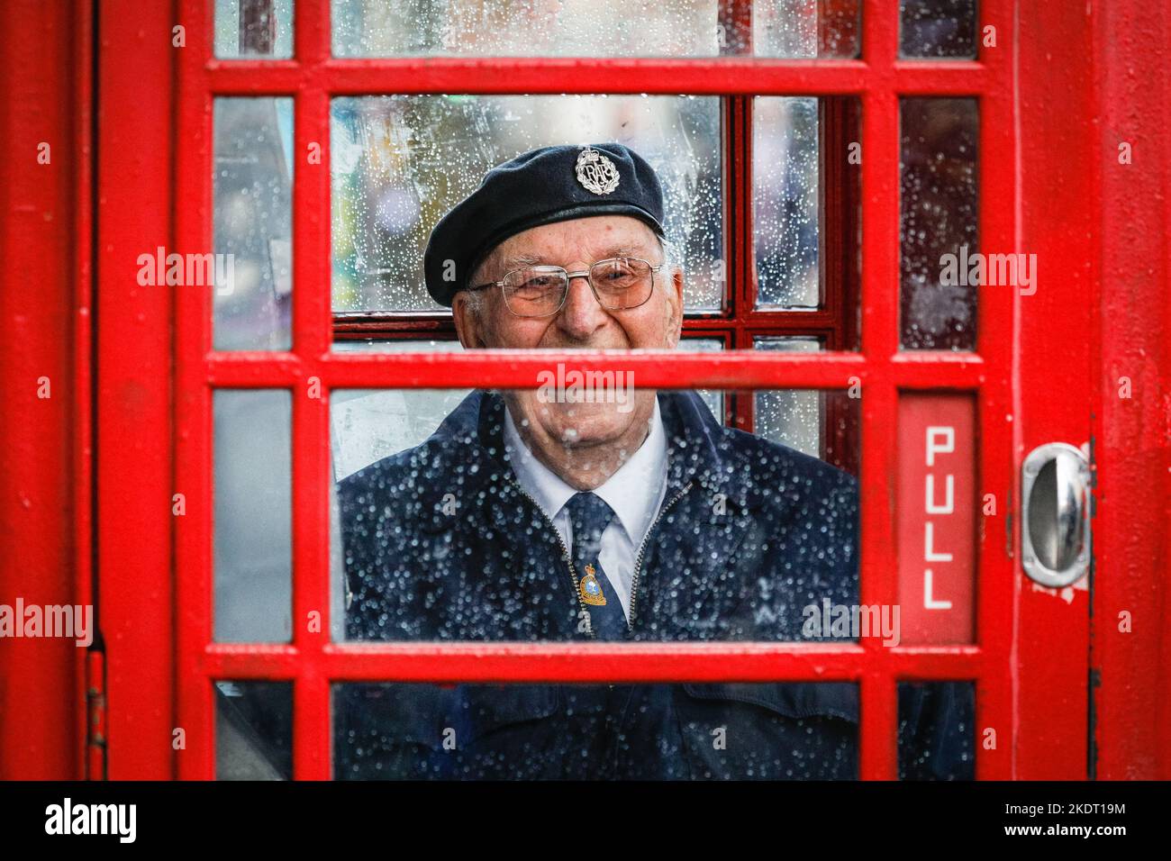 London, Großbritannien. 08.. November 2022. Ein britischer Militärveteran lächelt, als er sich in einer roten Londoner Telefonbox in Whitehall in der Nähe des Cenotaph vor dem starken Regen schützt. Kredit: Imageplotter/Alamy Live Nachrichten Stockfoto