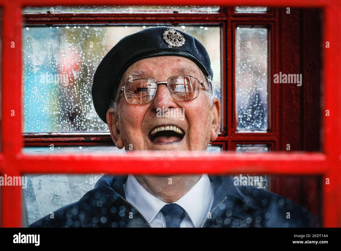 London, Großbritannien. 08.. November 2022. Ein britischer Militärveteran lächelt, als er sich in einer roten Londoner Telefonbox in Whitehall in der Nähe des Cenotaph vor dem starken Regen schützt. Kredit: Imageplotter/Alamy Live Nachrichten Stockfoto