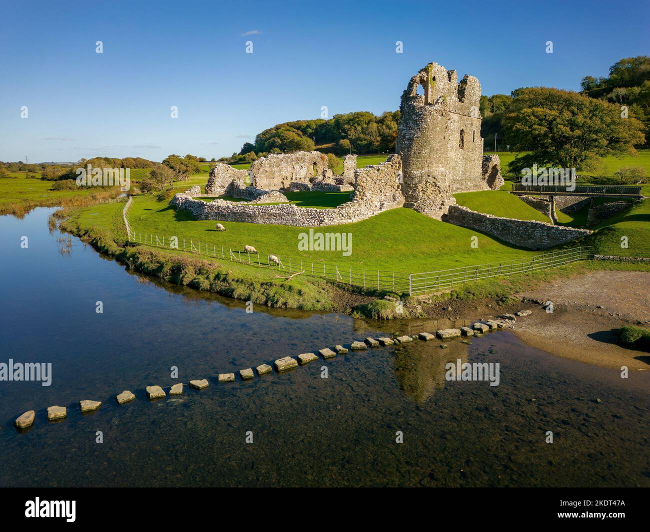 Luftaufnahme von Trittsteinen über einen kleinen Fluss, der zu den Ruinen einer alten Burg führt (Ogmore Castle, Glamorgan, Wales) Stockfoto