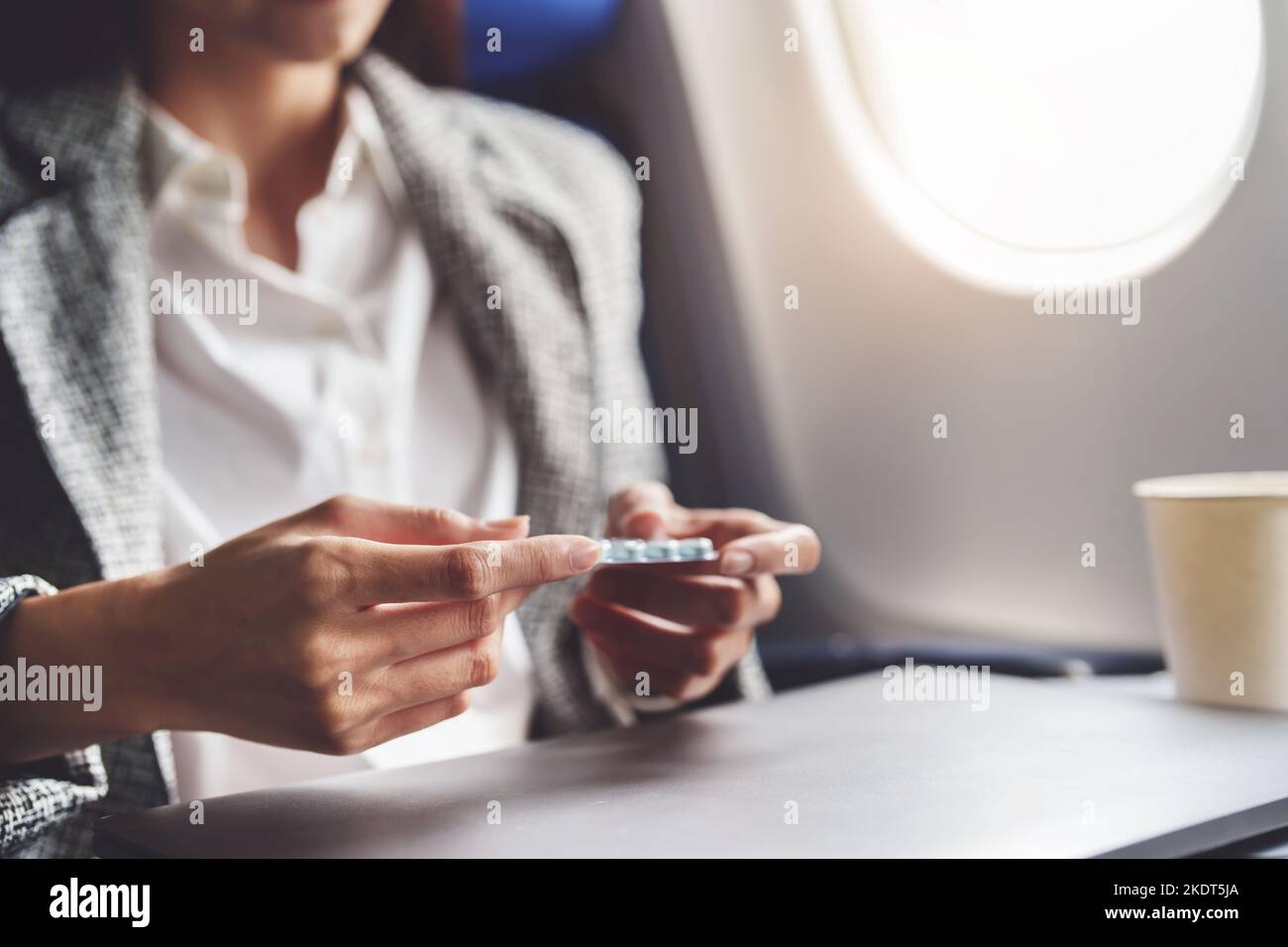 Eine erfolgreiche asiatische Geschäftsfrau oder Unternehmerin in einem formellen Anzug auf einem Flugzeug in der Business Class, die während des Fluges Flugpillen nimmt Stockfoto