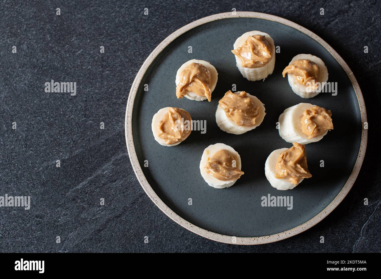 Banane mit Erdnussbutter - gesunder Snack isoliert auf dunklem Hintergrund von oben Stockfoto