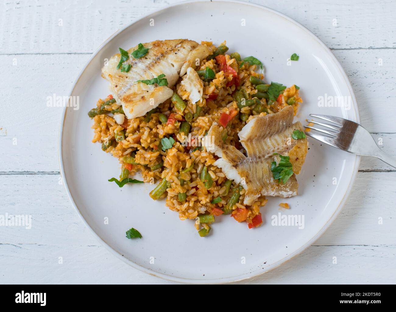 Fisch mit braunem Reis und Gemüse auf einem Teller isoliert auf weißem Hintergrund Stockfoto