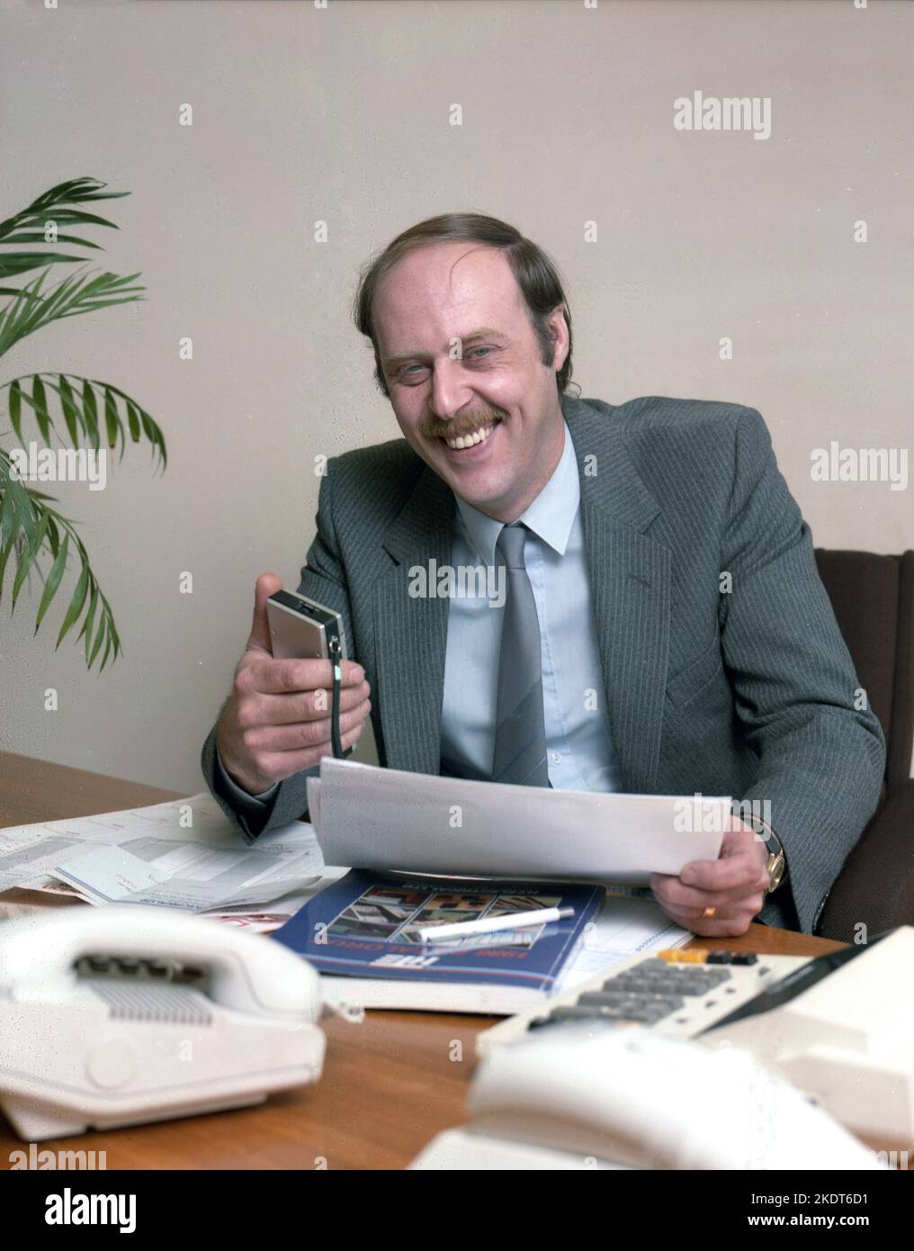 1980s, historisch, ein Geschäftsführer, der an seinem Schreibtisch sitzt, mit Papierkram und in der Hand, eine Diktatmaschine, England, Großbritannien. Stockfoto