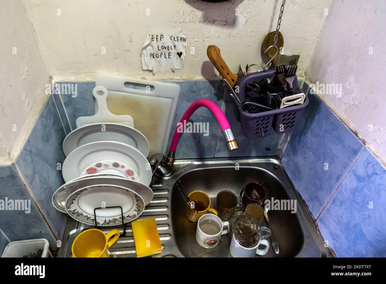 Dreckiges Geschirr, ungewaschen im Waschbecken mit einem Schild „Keep clean lovely people“. Thema - Gemeinschaftsküche, Gemeinschaftsraum. Stockfoto