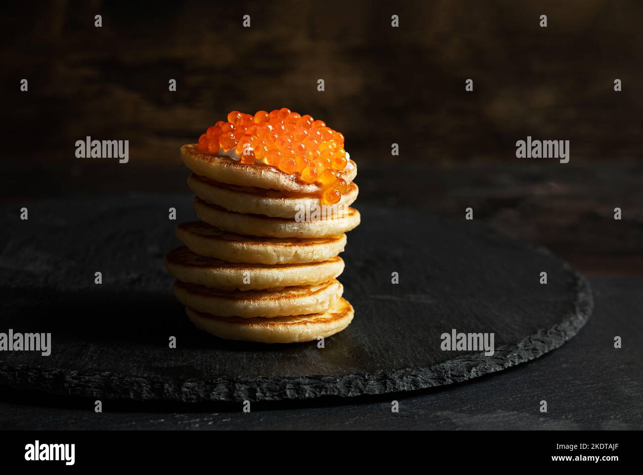 Roter Kaviar auf kleinen Pfannkuchen Blinis mit saurer Creme auf dunklem Hintergrund Stockfoto